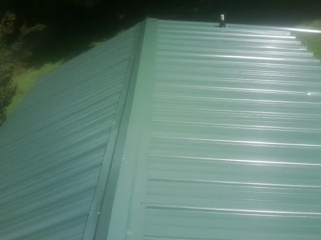New green metal panels meeting at the ridge of a roof — Flat Roof Repair work by our crew in New Lisbon