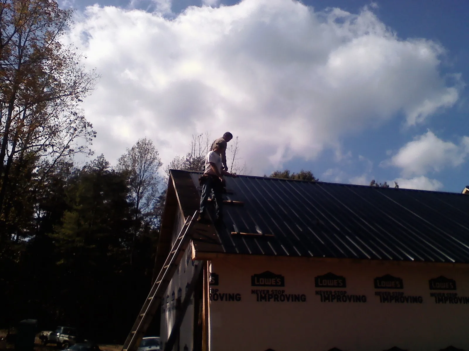 Roofer fastening dark metal panels high against a cloudy sky, from a Roof Inspection job in New Lisbon